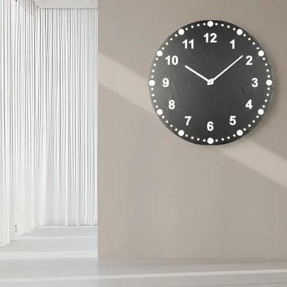 Round slate clock face with white numbers on a tiled wall background